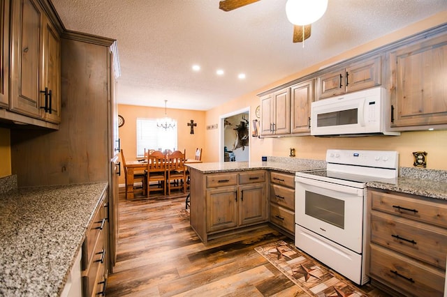 kitchen with kitchen peninsula, white appliances, ceiling fan with notable chandelier, dark wood-type flooring, and decorative light fixtures