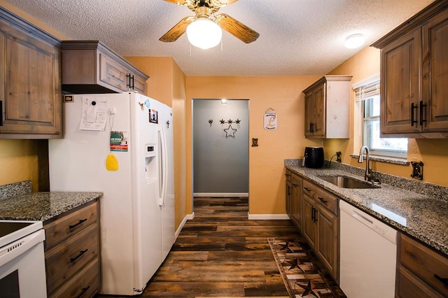 kitchen featuring dark stone counters, a textured ceiling, white appliances, dark wood-type flooring, and sink