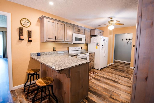 kitchen featuring a breakfast bar area, light stone counters, dark hardwood / wood-style flooring, and white appliances