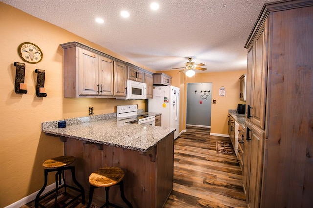 kitchen with a kitchen bar, a textured ceiling, dark wood-type flooring, and white appliances