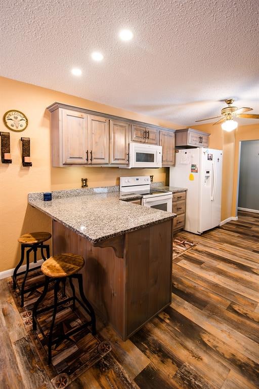 kitchen featuring a textured ceiling, kitchen peninsula, dark wood-type flooring, and white appliances