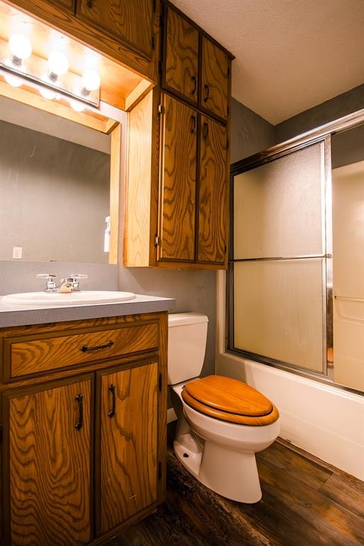 full bathroom with vanity, a textured ceiling, wood-type flooring, enclosed tub / shower combo, and toilet