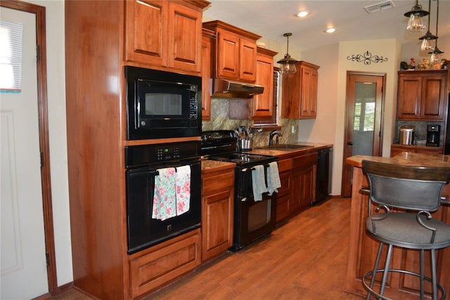 kitchen with hardwood / wood-style floors, backsplash, black appliances, sink, and decorative light fixtures