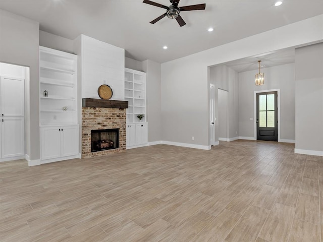 unfurnished living room with built in shelves, a fireplace, light hardwood / wood-style floors, and ceiling fan with notable chandelier