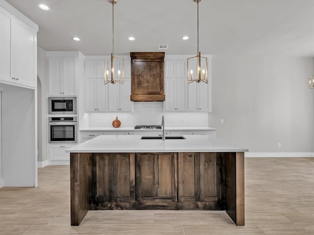 kitchen featuring a kitchen island with sink, sink, oven, and hanging light fixtures