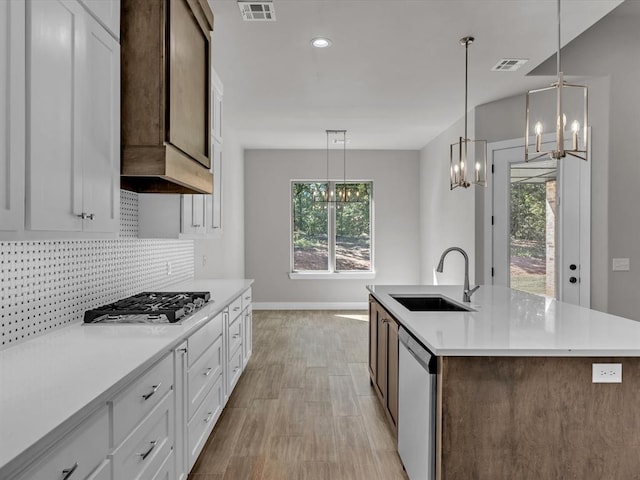 kitchen with stainless steel appliances, white cabinetry, sink, and a kitchen island with sink