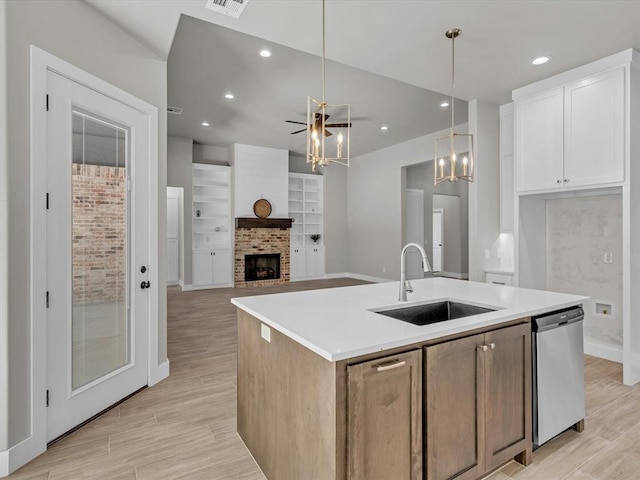 kitchen featuring white cabinetry, sink, stainless steel dishwasher, decorative light fixtures, and a kitchen island with sink