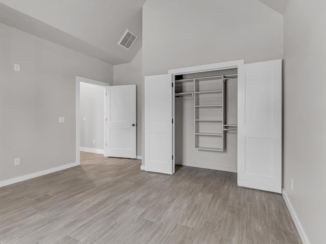 unfurnished bedroom with light wood-type flooring, high vaulted ceiling, and a closet