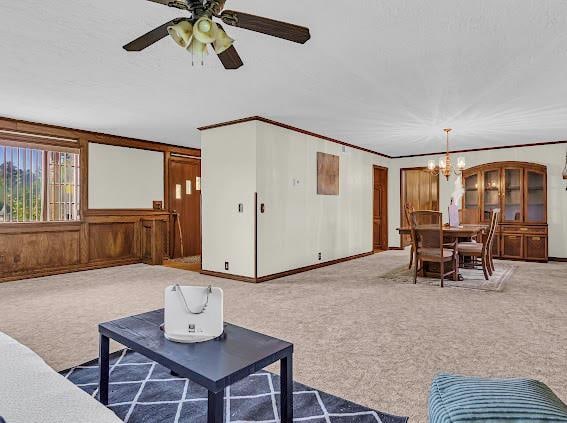 carpeted living room with ceiling fan with notable chandelier and ornamental molding