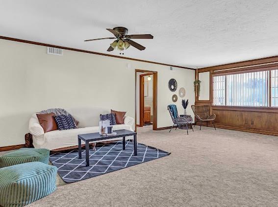 carpeted living room with a textured ceiling, ceiling fan, and crown molding