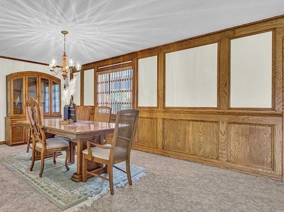 dining space with light carpet, wood walls, and a notable chandelier