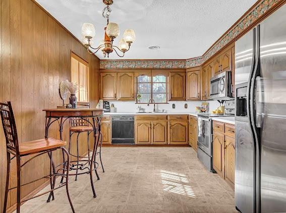 kitchen featuring appliances with stainless steel finishes, wooden walls, sink, pendant lighting, and a notable chandelier