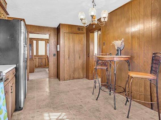 interior space with a chandelier, pendant lighting, stainless steel refrigerator, and wood walls