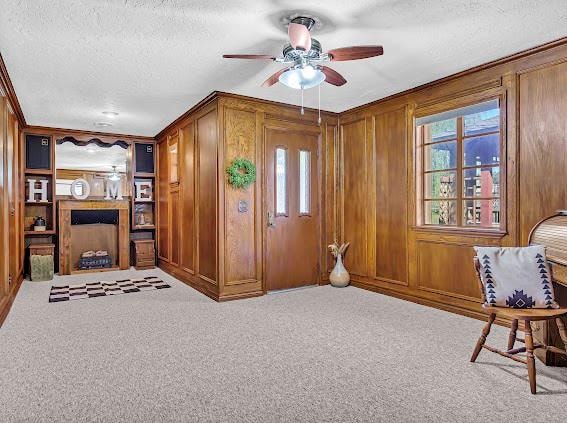 interior space with wooden walls, ceiling fan, light carpet, and a textured ceiling