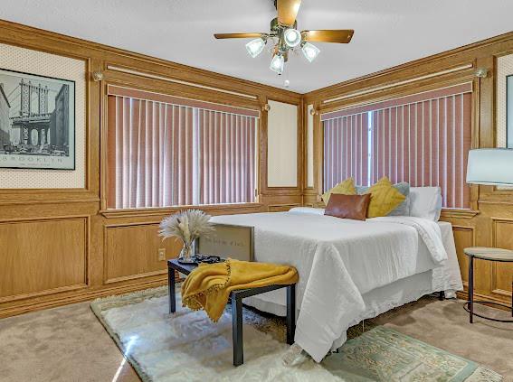 bedroom featuring ceiling fan, carpet, and wood walls