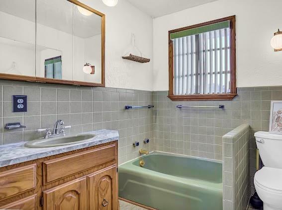 bathroom featuring vanity, toilet, a bath, and tile walls