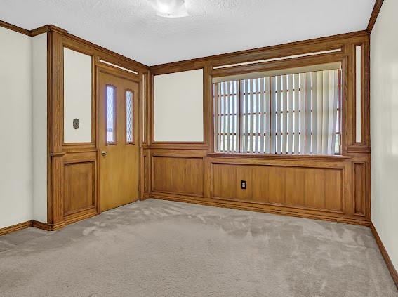 entryway with light colored carpet, ornamental molding, a textured ceiling, and wooden walls