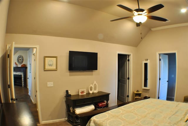 bedroom with dark wood-type flooring, a stone fireplace, vaulted ceiling, ceiling fan, and ornamental molding