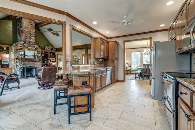 kitchen featuring appliances with stainless steel finishes, a fireplace, ceiling fan with notable chandelier, and light stone counters