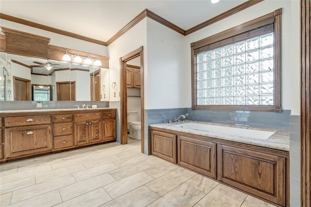 full bath featuring vanity, toilet, a ceiling fan, ornamental molding, and a garden tub