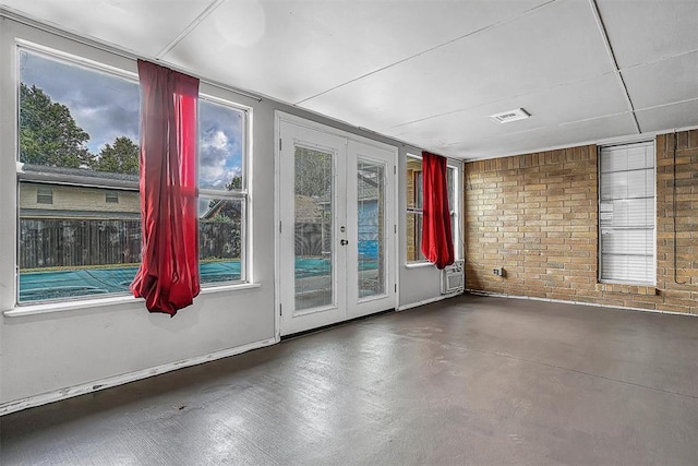 unfurnished room with brick wall, concrete floors, visible vents, and french doors