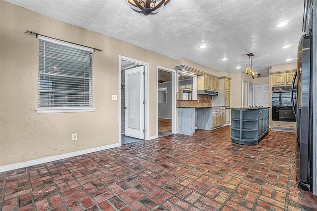 kitchen with a center island, decorative light fixtures, dark countertops, cream cabinets, and baseboards