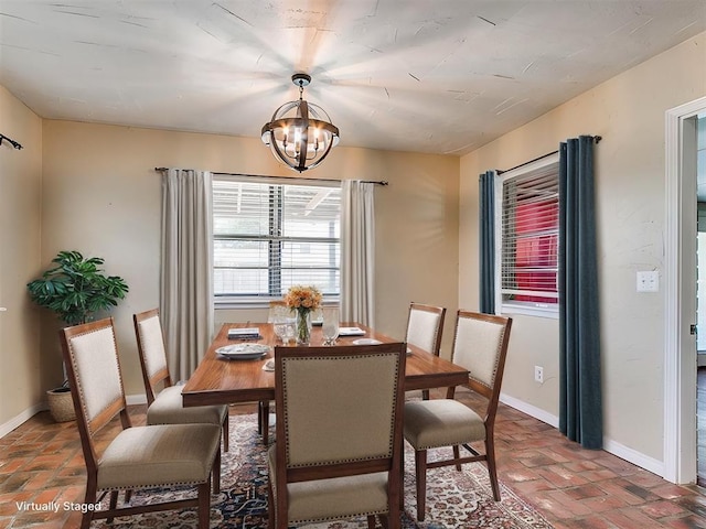 dining area featuring brick floor, baseboards, and a chandelier