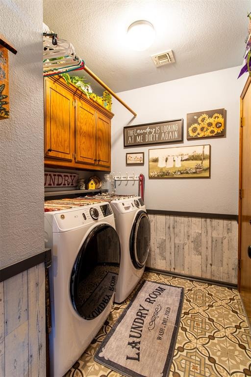 washroom with washing machine and clothes dryer, wooden walls, cabinets, and a textured ceiling