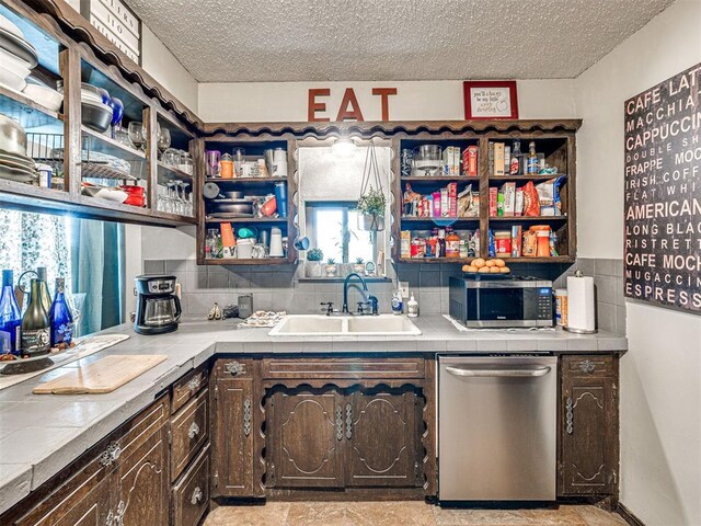 kitchen with tile countertops, sink, a textured ceiling, dark brown cabinets, and stainless steel appliances