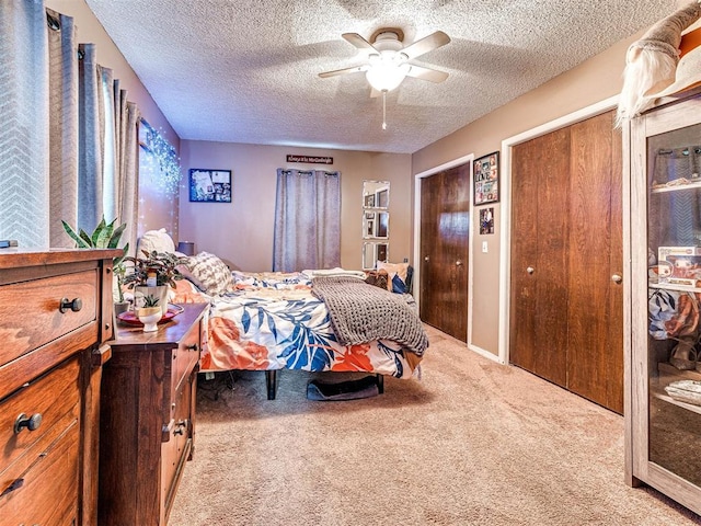 carpeted bedroom featuring ceiling fan, a textured ceiling, and two closets