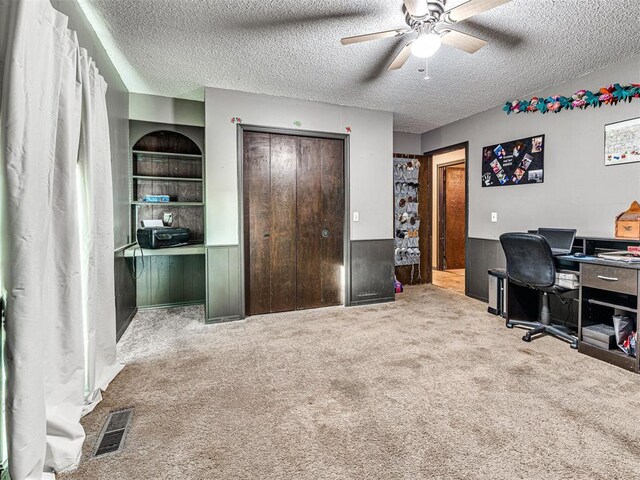 carpeted home office with a textured ceiling, built in features, and ceiling fan