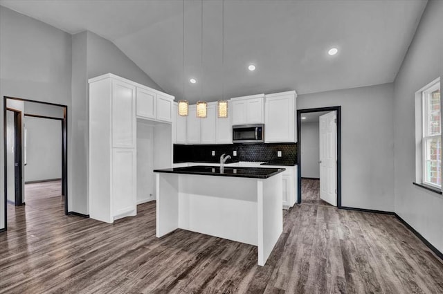 kitchen with dark hardwood / wood-style flooring, an island with sink, hanging light fixtures, and lofted ceiling