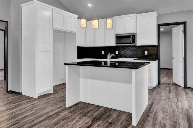 kitchen featuring hardwood / wood-style flooring, decorative light fixtures, white cabinetry, and an island with sink