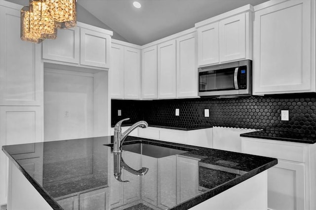 kitchen with white cabinets, hanging light fixtures, lofted ceiling, and dark stone countertops