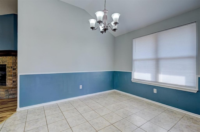 spare room featuring a fireplace, an inviting chandelier, lofted ceiling, and light tile patterned flooring