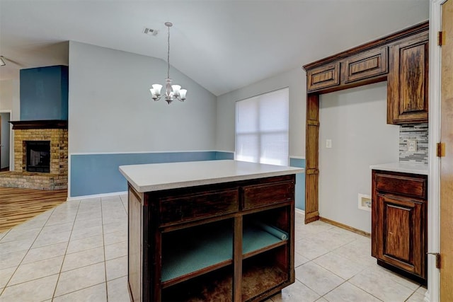 kitchen with an inviting chandelier, light tile patterned flooring, vaulted ceiling, a fireplace, and a kitchen island