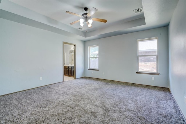 carpeted spare room featuring plenty of natural light, ceiling fan, and a raised ceiling