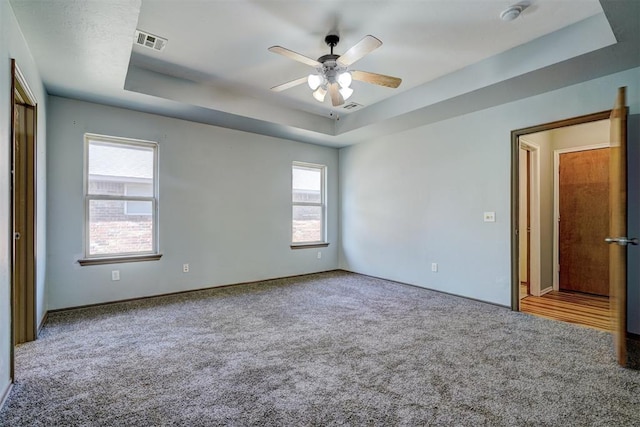 unfurnished room with a tray ceiling, ceiling fan, carpet floors, and a healthy amount of sunlight