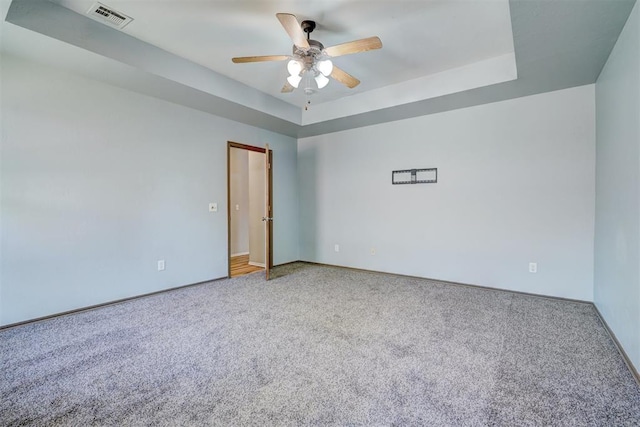 unfurnished room with a raised ceiling, ceiling fan, and carpet floors