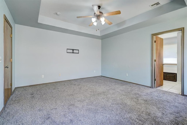 carpeted spare room featuring a tray ceiling and ceiling fan