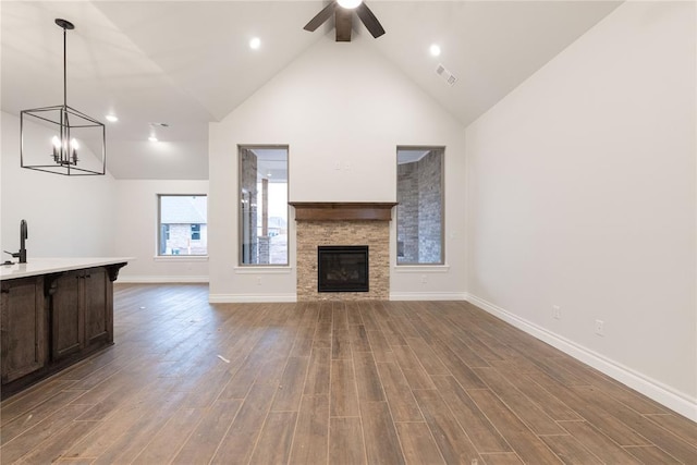 unfurnished living room with visible vents, a stone fireplace, wood finished floors, and a ceiling fan