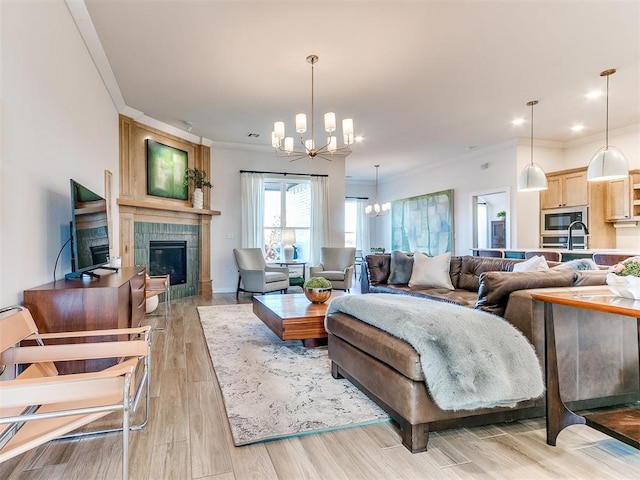 living room with a fireplace, sink, ornamental molding, an inviting chandelier, and light hardwood / wood-style flooring