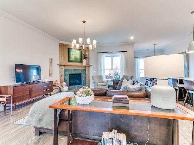 living room with crown molding, light wood-type flooring, a notable chandelier, and a fireplace