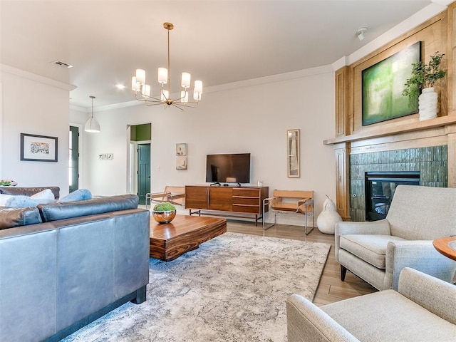 living room featuring ornamental molding, a tile fireplace, a chandelier, and light wood-type flooring