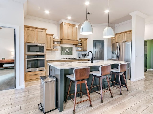 kitchen with pendant lighting, appliances with stainless steel finishes, a kitchen breakfast bar, tasteful backsplash, and a center island with sink