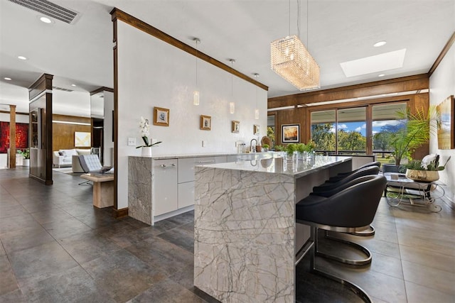 kitchen with wood walls, white cabinets, a skylight, light stone countertops, and decorative light fixtures