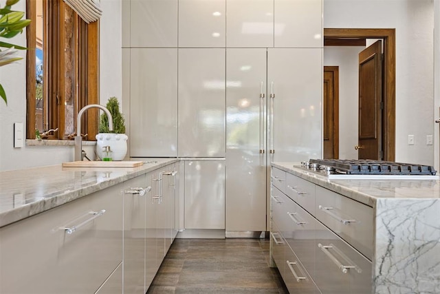 kitchen with white cabinets, sink, dark hardwood / wood-style floors, light stone countertops, and stainless steel gas cooktop