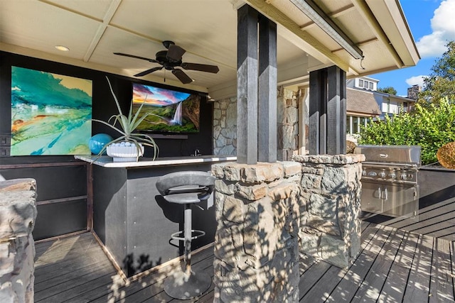 wooden terrace featuring area for grilling, an outdoor bar, ceiling fan, and exterior kitchen