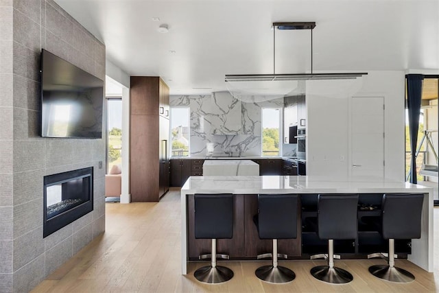 kitchen with pendant lighting, light hardwood / wood-style floors, a breakfast bar area, and a tiled fireplace