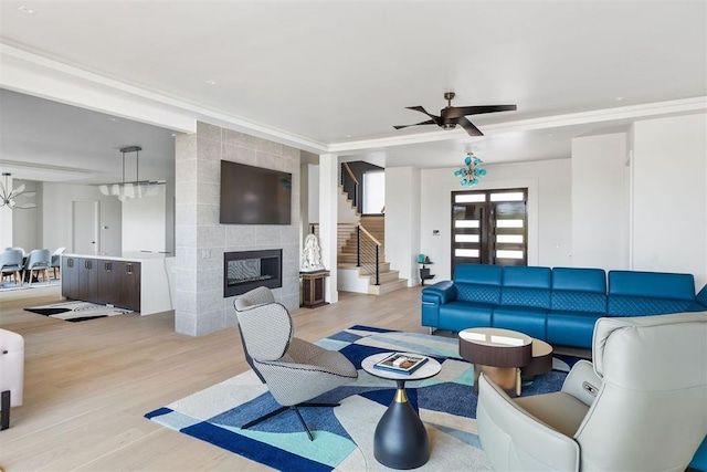 living room with a tiled fireplace, ceiling fan, and light wood-type flooring